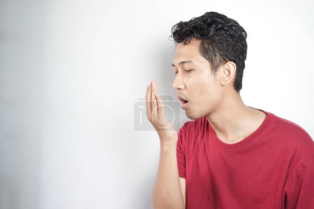 Photo for A man checks for bad breath and breathes with his hands. he has bad breath Concept of oral and dental health - Royalty Free Image
