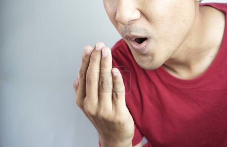 Téléchargez les photos : A man checks for bad breath and breathes with his hands. he has bad breath Concept of oral and dental health - en image libre de droit