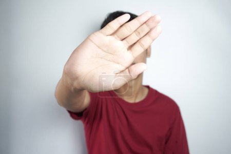 Photo for Young asian man putting hand up front to stop camera, refusing photos or pictures against flat color wall - Royalty Free Image
