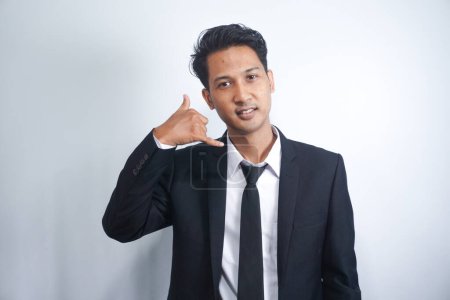 Photo for A photo of good-looking young man in suit isolated on white background making a gesture "call me" with his fingers - Royalty Free Image