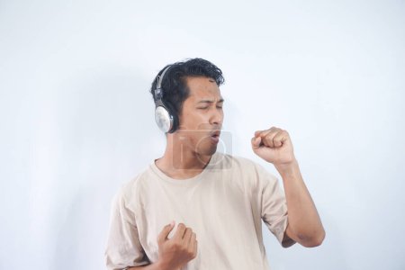 Photo for Energized man sings to music, moves actively, wears headphones and casual t shirt, poses against white background, keeps mouth widely opened, enjoys life, isolated on white studio wall - Royalty Free Image