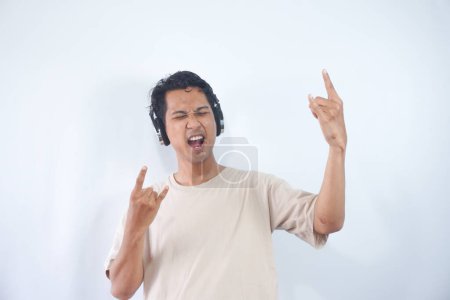 Photo for Upbeat man enjoys life, goes wild with nice music, has fun, raises arms, clenches fists while moves with rhythm, wears modern stereo headphones on ears, sings favourite song - Royalty Free Image