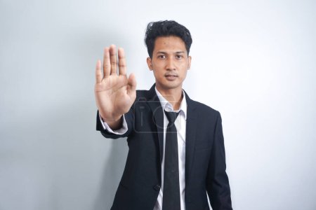 Photo for Serious Asian man gesturing STOP, showing palm to camera over grey studio background. Young man expressing his negative attitude, rejecting or prohibiting something - Royalty Free Image