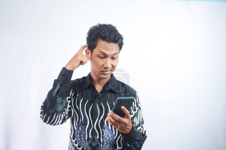 Photo for Portrait of handsome young adult with dreamy look, thinking while holding smartphone, isolated over white background. - Royalty Free Image
