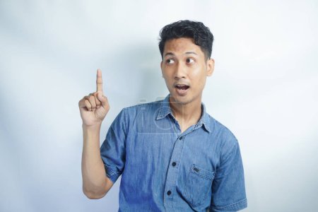 Photo for Cute assertive dark-haired asian man wear blue shirt raise hands up, showing promo, pointing fingers up, grinning, inviting use link, try-out product, give direction, stand purple background - Royalty Free Image