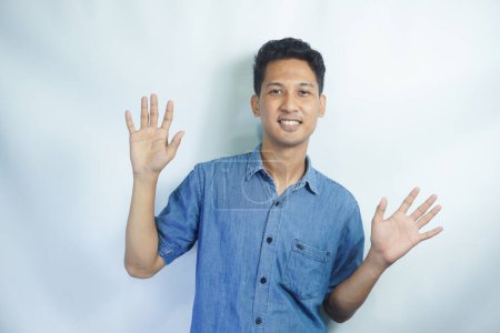Photo for Studio portrait shot of Asian happy young handsome smart teenager teen guy model in blue shirt smiling show teeth look at camera waving hand greeting say hello hi of goodbye on white background - Royalty Free Image