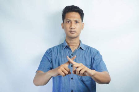 Photo for Asian person showing x shape gesture with hands, expressing refusal and disagreement. Young male model showing no symbol and rejection, refusing to listen over white backdrop. - Royalty Free Image