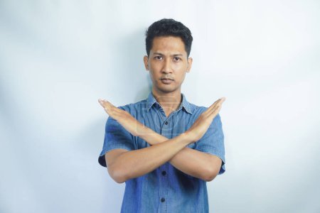 Photo for Asian person showing x shape gesture with hands, expressing refusal and disagreement. Young male model showing no symbol and rejection, refusing to listen over white backdrop. - Royalty Free Image
