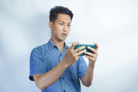 Foto de Joven hombre asiático jugando un videojuego en el teléfono móvil y obtuvo reacciones negativas. Las expresiones faciales pueden ser furiosas, feroces, molestas, infelices, irritadas, frustradas. - Imagen libre de derechos