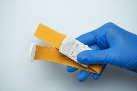 Photo for Doctor wearing blue medical gloves holding a yellow tourniquet, isolated on white - Royalty Free Image