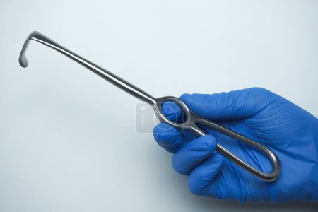 Téléchargez les photos : Le médecin portant des gants médicaux bleus tient Langenbeck, un outil chirurgical communément appelé un crochet qui est utilisé pour crocheter l'incision afin qu'elle s'ouvre large - en image libre de droit