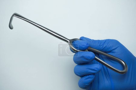 Téléchargez les photos : Le médecin portant des gants médicaux bleus tient Langenbeck, un outil chirurgical communément appelé un crochet qui est utilisé pour crocheter l'incision afin qu'elle s'ouvre large - en image libre de droit