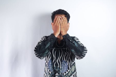 Foto de Asiático hombre vistiendo batik llorando y cubriendo su cara con ambos manos - Imagen libre de derechos