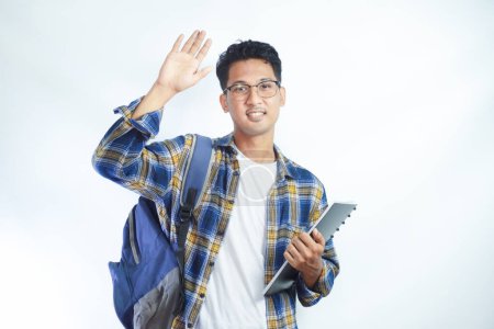 Photo for Asian teenager wearing student backpack and holding books waiving saying hello happy and smiling, friendly welcome gesture - Royalty Free Image