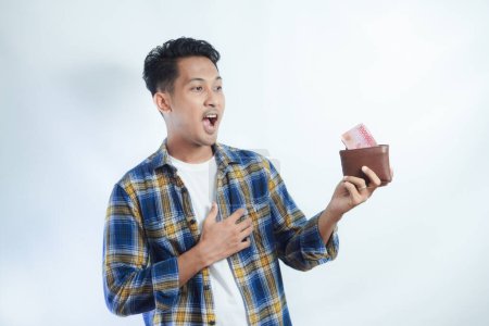 Téléchargez les photos : Adulte asiatique homme montrant l'expression étonnante tout en tenant son portefeuille plein d'argent - en image libre de droit