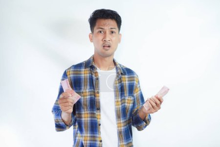 Erwachsener asiatischer Mann zeigt enttäuschten Gesichtsausdruck, während seine beiden Hände Papiergeld halten