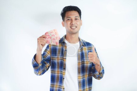 Nahaufnahme Porträt eines erwachsenen asiatischen Mannes gibt den Daumen nach oben, während er Geld hält und einen glücklichen Gesichtsausdruck zeigt