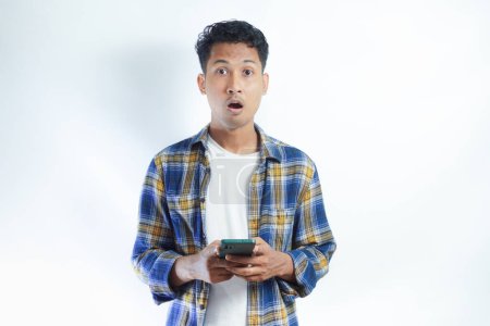Hombre asiático adulto mirando a la cámara con expresión impactada mientras sostiene el teléfono