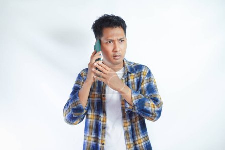 Photo for Adult Asian man showing worried expression during a phone call - Royalty Free Image