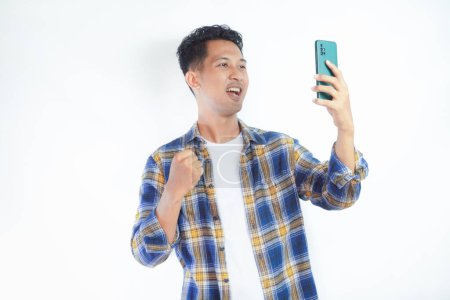 Photo for Adult Asian man showing happy gesture while looking to his mobile phone - Royalty Free Image