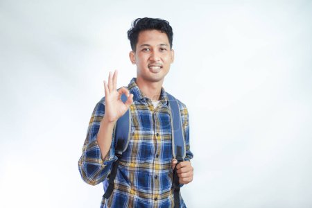 Photo for Smiling happy young Asian boy student wearing casual clothes and backpack showing ok sign, making approval gesture with finger isolated on white background. high school university college concept - Royalty Free Image
