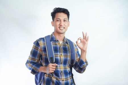 Photo for Smiling happy young Asian boy student wearing casual clothes and backpack showing ok sign, making approval gesture with finger isolated on white background. high school university college concept - Royalty Free Image