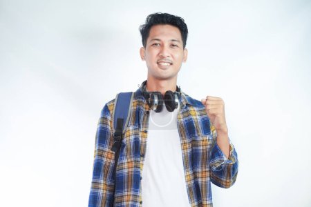 Photo for Excited young Asian man wearing casual clothes and glasses backpack earphone standing while celebrating success isolated on white background. high school university college concept - Royalty Free Image