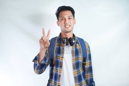 Photo for Asian man student smiling at the camera and doing two fingers sign - Royalty Free Image