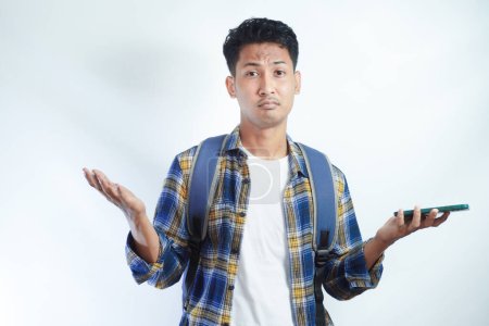 Téléchargez les photos : Un jeune étudiant asiatique perplexe ne sait pas quoi faire sur fond blanc dans un studio isolé sur fond blanc. École secondaire université concept collège - en image libre de droit