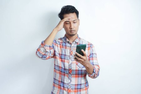Photo for Asian man holding his mobile phone with sad expression - Royalty Free Image