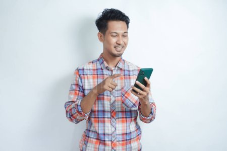 Photo for Adult Asian man smiling happy while pointing to mobile phone that he hold - Royalty Free Image