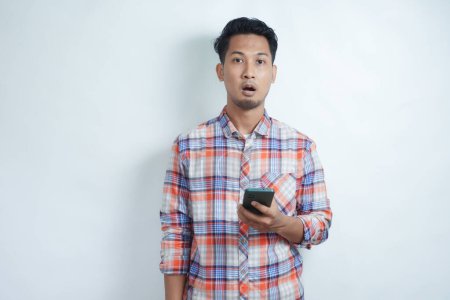 Erwachsener asiatischer Mann blickt mit schockiertem Gesichtsausdruck in die Kamera, während er sein Handy hält