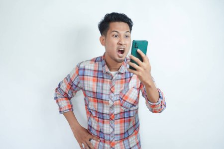 Photo for Adult Asian man showing rage expression when looking to his cellular phone - Royalty Free Image