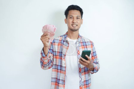 Adult Asian man holding money and mobile phone smiling happy at the camera
