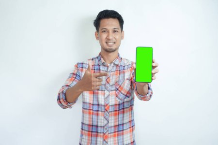 Foto de Adulto asiático hombre sonriendo feliz mientras muestra verde pantalla del teléfono móvil y apuntando a ella - Imagen libre de derechos