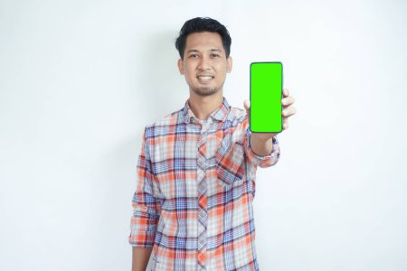 Photo for Adult Asian man standing while smiling showing green mobile phone screen that he hold - Royalty Free Image