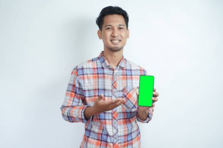 Foto de Adulto asiático hombre sonriendo feliz mientras muestra verde pantalla del teléfono móvil y apuntando a ella - Imagen libre de derechos
