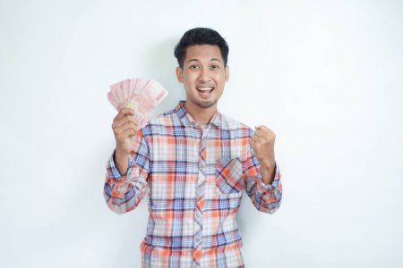Foto de Adulto asiático hombre apretado puño mientras sosteniendo papel moneda y mostrando feliz expresión - Imagen libre de derechos