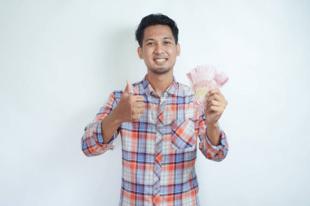 Nahaufnahme Porträt eines erwachsenen asiatischen Mannes gibt den Daumen nach oben, während er Geld hält und einen glücklichen Gesichtsausdruck zeigt