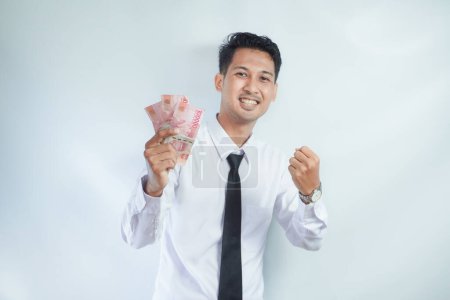 Adulto asiático hombre apretado puño mientras sosteniendo papel moneda y mostrando feliz expresión