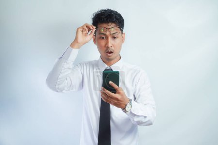 Photo for Adult Asian man looking to mobile phone that he hold with surprised expression - Royalty Free Image