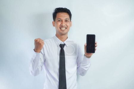 Photo for Adult Asian man clenched fist with excited expression while showing blank mobile phone screen - Royalty Free Image