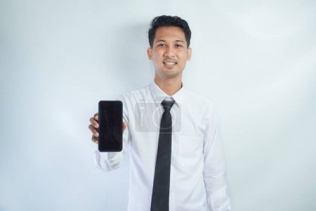 Photo for Adult Asian man standing while smiling showing blank mobile phone screen that he hold - Royalty Free Image