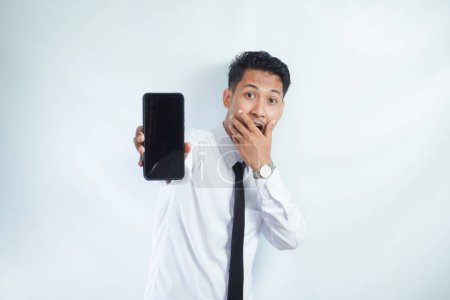 Hombre asiático adulto de pie mientras sonríe mostrando la pantalla del teléfono móvil en blanco que sostiene