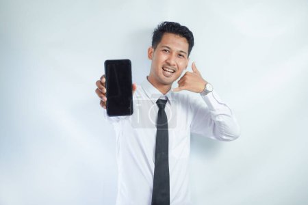 Hombre asiático adulto de pie mientras sonríe mostrando la pantalla del teléfono móvil en blanco que sostiene