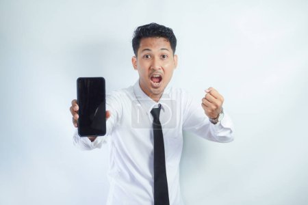 Photo for Adult Asian man clenched fist with excited expression while showing blank mobile phone screen - Royalty Free Image