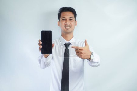 Adulto asiático hombre sonriendo confiado mientras señala el dedo a la pantalla del teléfono en blanco
