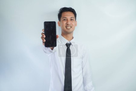 Erwachsener asiatischer Mann steht lächelnd und zeigt leeren Handybildschirm, den er in der Hand hält