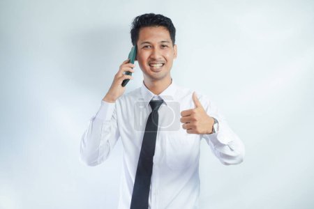 Photo for Adult Asian man smiling and give thumb up while answering a phone call - Royalty Free Image
