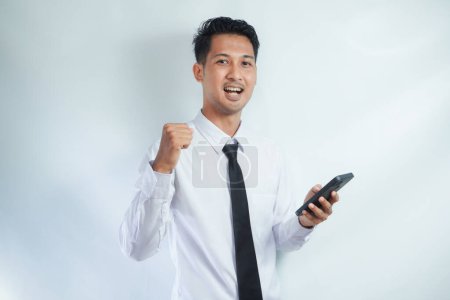 Photo for Adult Asian man looking camera while holding mobile phone showing enthusiastic expression - Royalty Free Image
